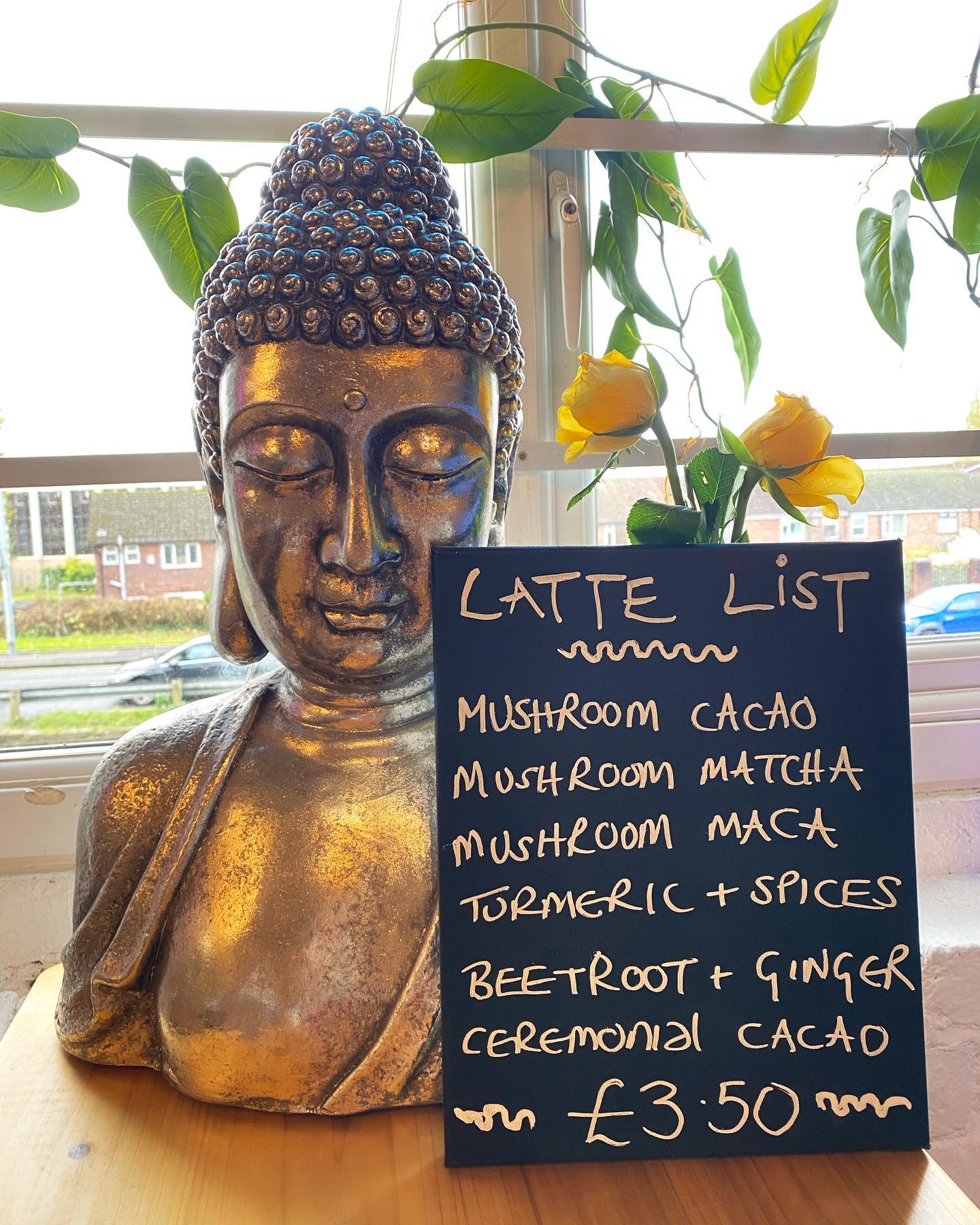 Handwritten latte list chalkboard beside a Buddha statue